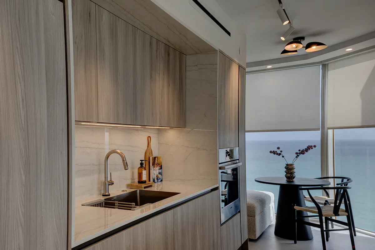 Kitchen with stone backsplash and wall ovens, breakfast table in the window over the ocean